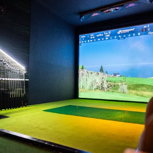 Baie de practice couverte du Par 4 à Mérignac, tapis de frappe face à un écran de simulation et râtelier de clubs